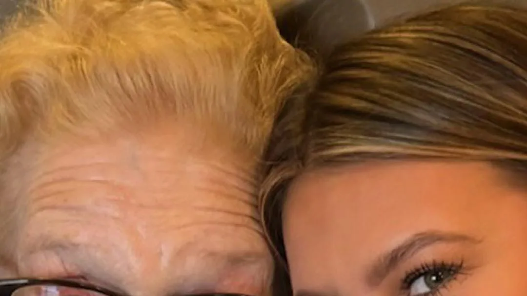 Close-up selfie of an older woman with curly blonde hair and glasses, head to head with a young woman with highlighted hair