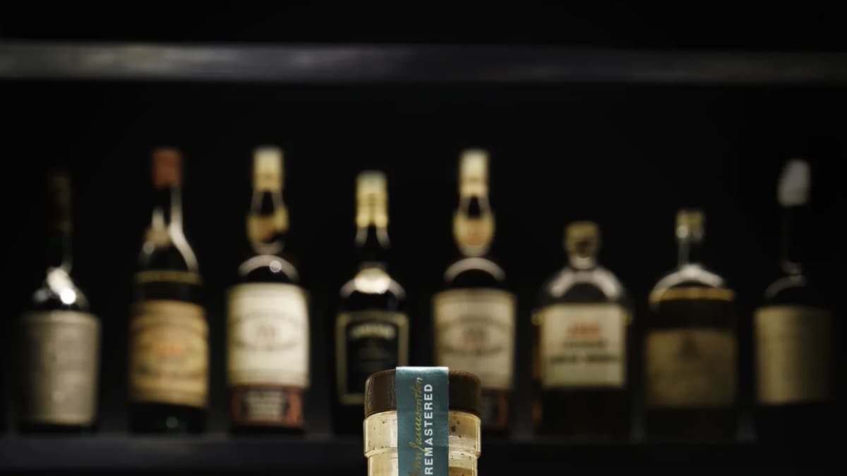 Jameson bottle neck with a teal "REMASTERED" seal in front of a dark shelf of blurred vintage whiskey bottles