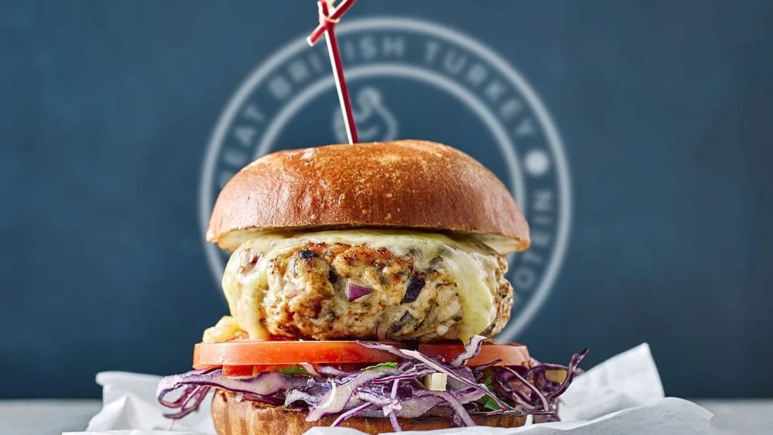 Turkey burger with melted cheese, tomato and red cabbage in a brioche bun before a blue logo reading "BRITISH TURKEY"