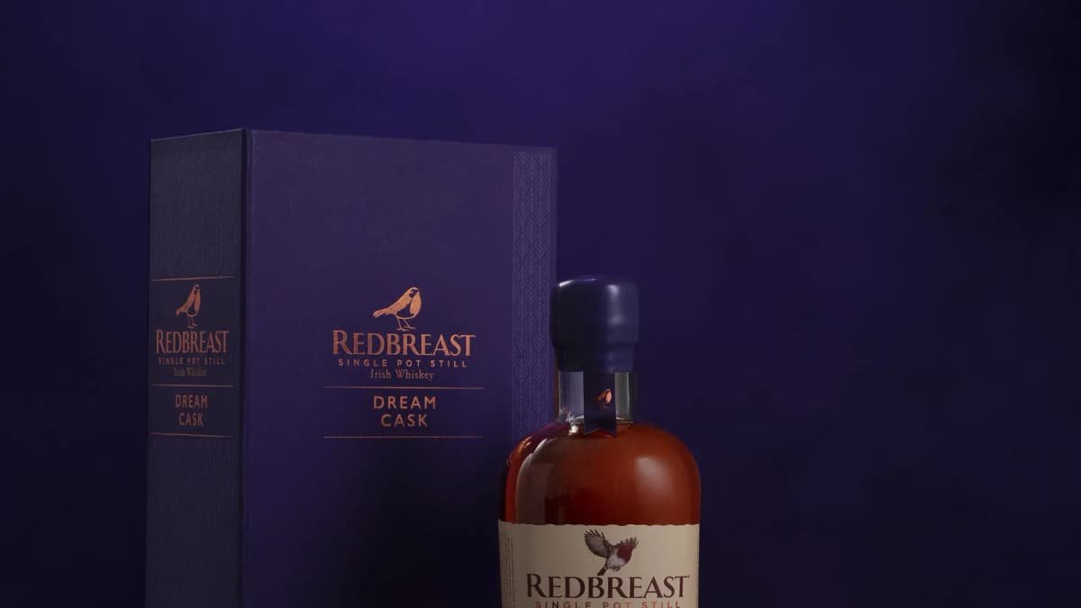 Redbreast whiskey bottle with a wax-sealed top beside a navy box printed "DREAM CASK" against a dark purple backdrop