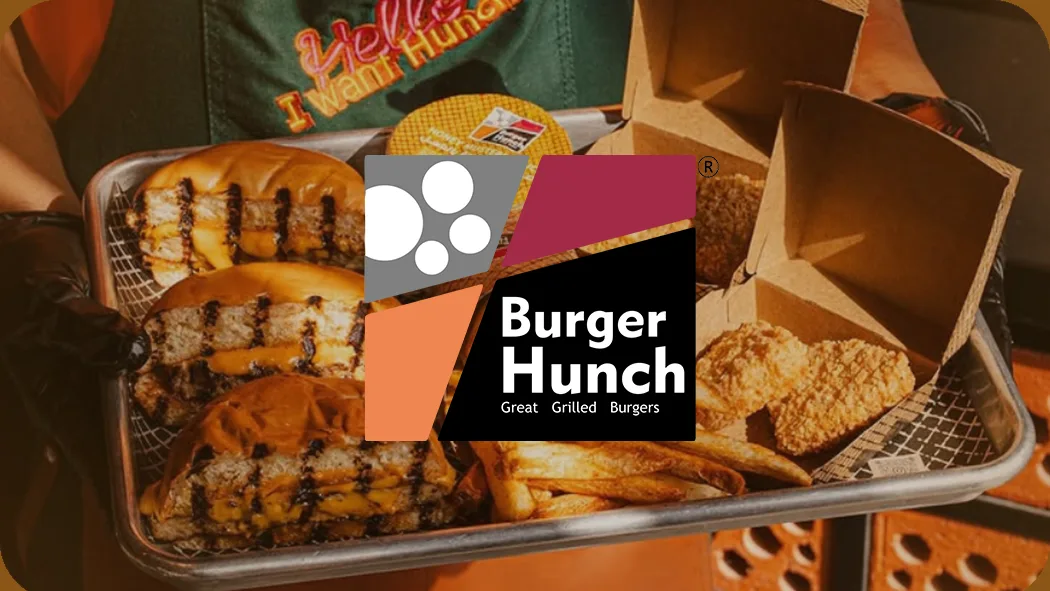 Gloved hands hold a tray of grilled burgers, fries and fried chicken behind a "Burger Hunch Great Grilled Burgers" logo
