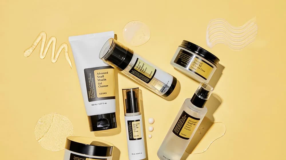 COSRX "Advanced Snail 96 Mucin Power Essence", cleanser tube and creams on yellow with gel and cream smears