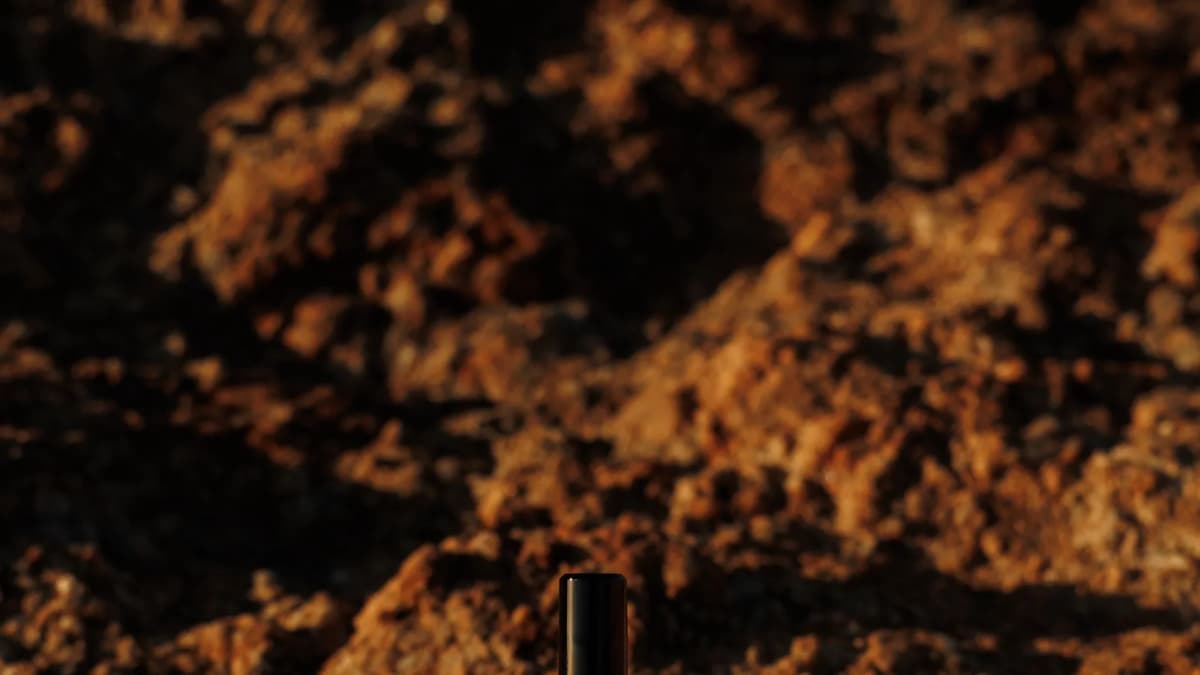 Serge Lutens, fragrance bottle standing on red-brown rock in low light
