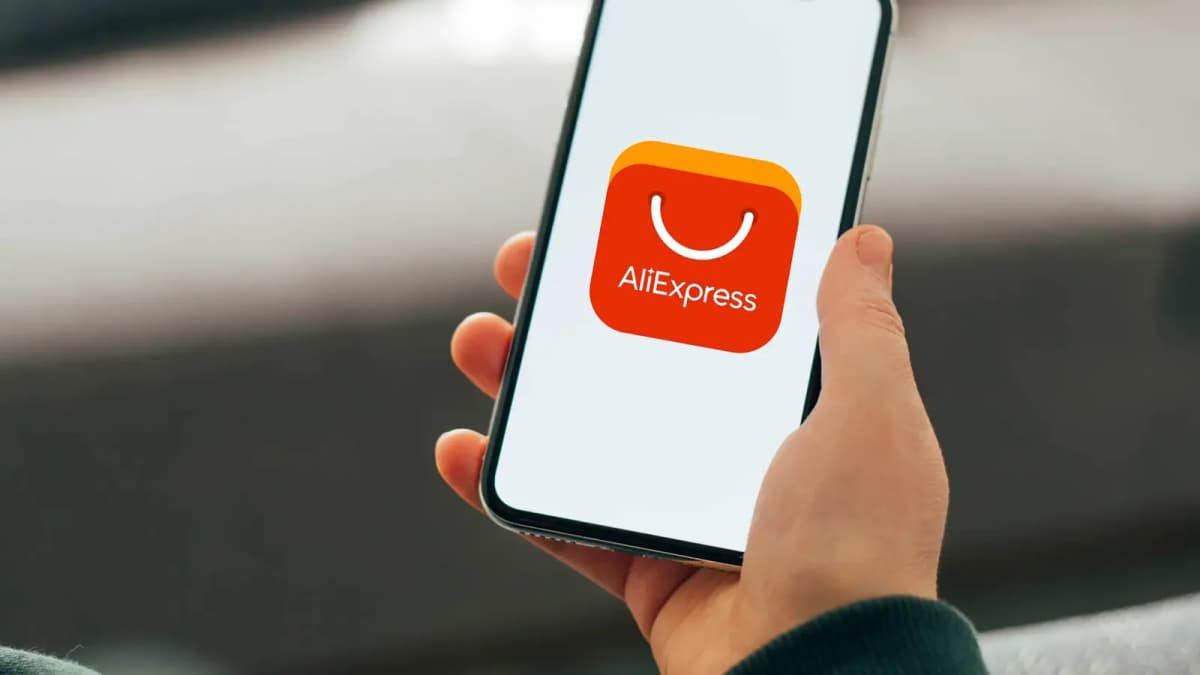 A hand holds a smartphone showing the red-orange AliExpress app logo with the word "AliExpress" on a white screen