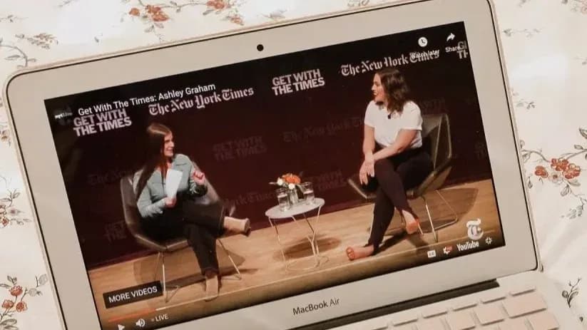 Laptop plays video of two women seated onstage talking before a New York Times "GET WITH THE TIMES" backdrop