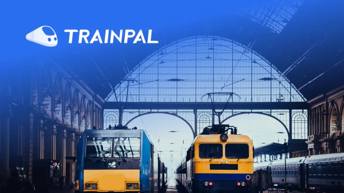 TrainPal logo over two blue and yellow locomotives parked beneath the arched glass and iron roof of a train station
