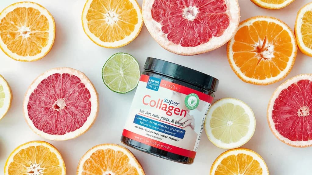 Jar of NeoCell "Super Collagen" powder lying among halved grapefruits, oranges, a lemon and a lime on a white surface