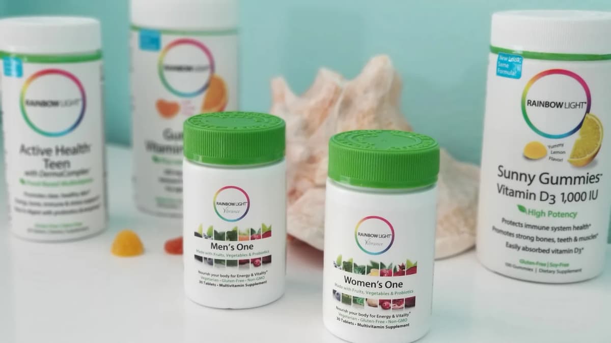 Rainbow Light "Men's One", "Women's One" and "Sunny Gummies" bottles beside a conch shell and gummies on a white table