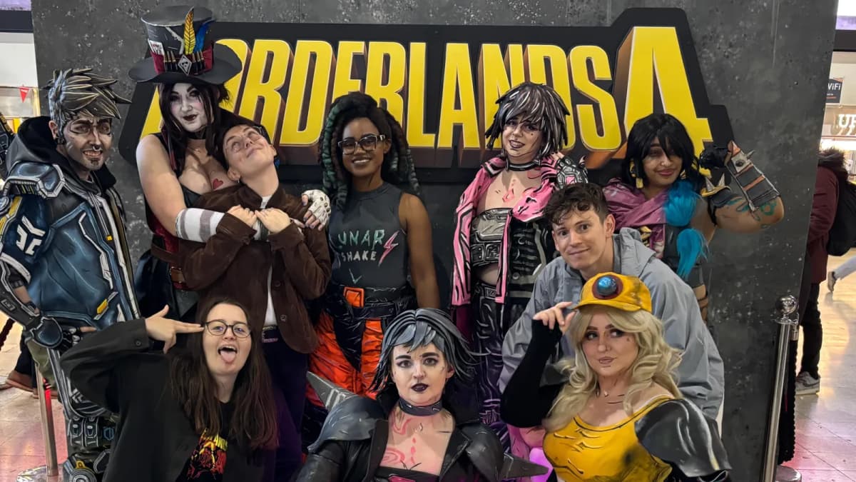 Ten people, some in comic-style costumes with painted faces, pose and pull faces indoors beneath a large Borderlands 4 logo