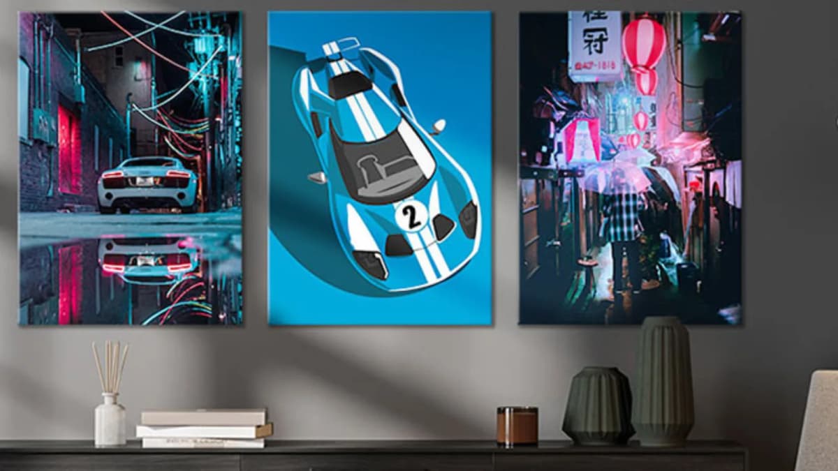 Three metal posters on a gray wall: a white sports car in a neon alley, a blue race car, a rainy lantern-lit street