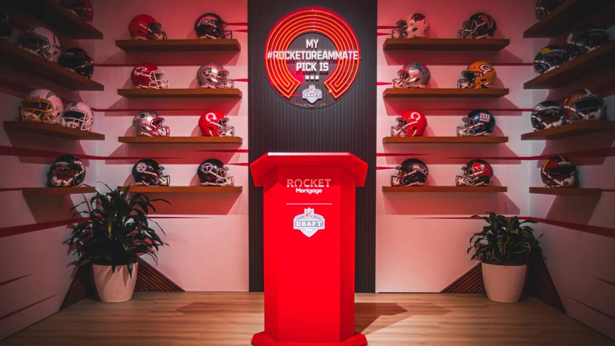 Red Rocket Mortgage podium before a neon "MY #ROCKETDREAMMATE PICK IS..." sign and shelves of football helmets