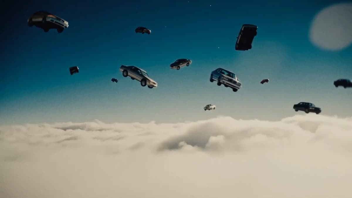Dozens of sedan cars float in a deep blue sky above a thick layer of white clouds, with a pale moon at upper right