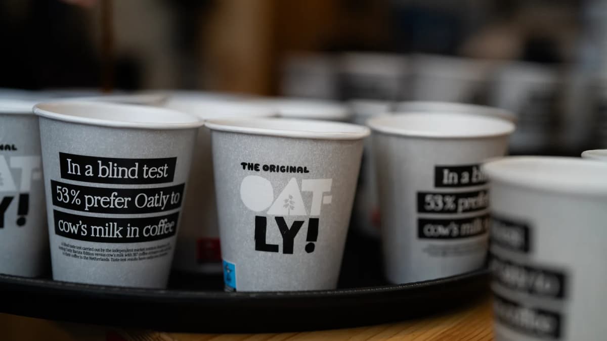 Oatly paper cups on a black tray, printed "In a blind test 53% prefer Oatly to cow’s milk in coffee"