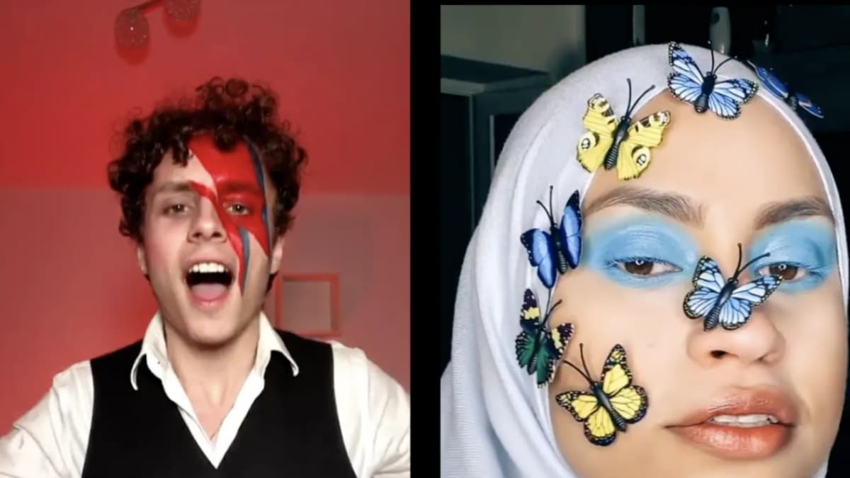 Curly-haired man with lightning bolt face paint singing beside woman in white hijab with butterflies on her face