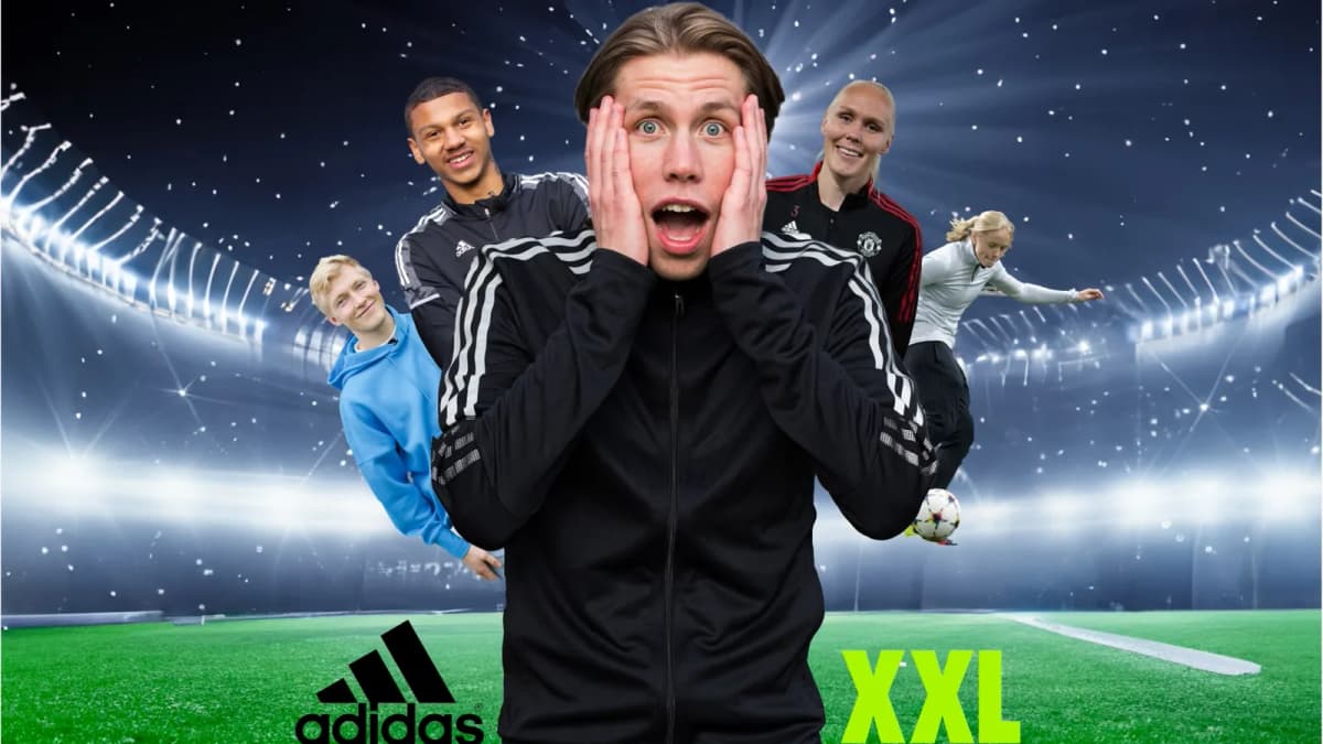 Shocked man in a black Adidas track jacket, hands on cheeks, with four smiling footballers in a floodlit stadium