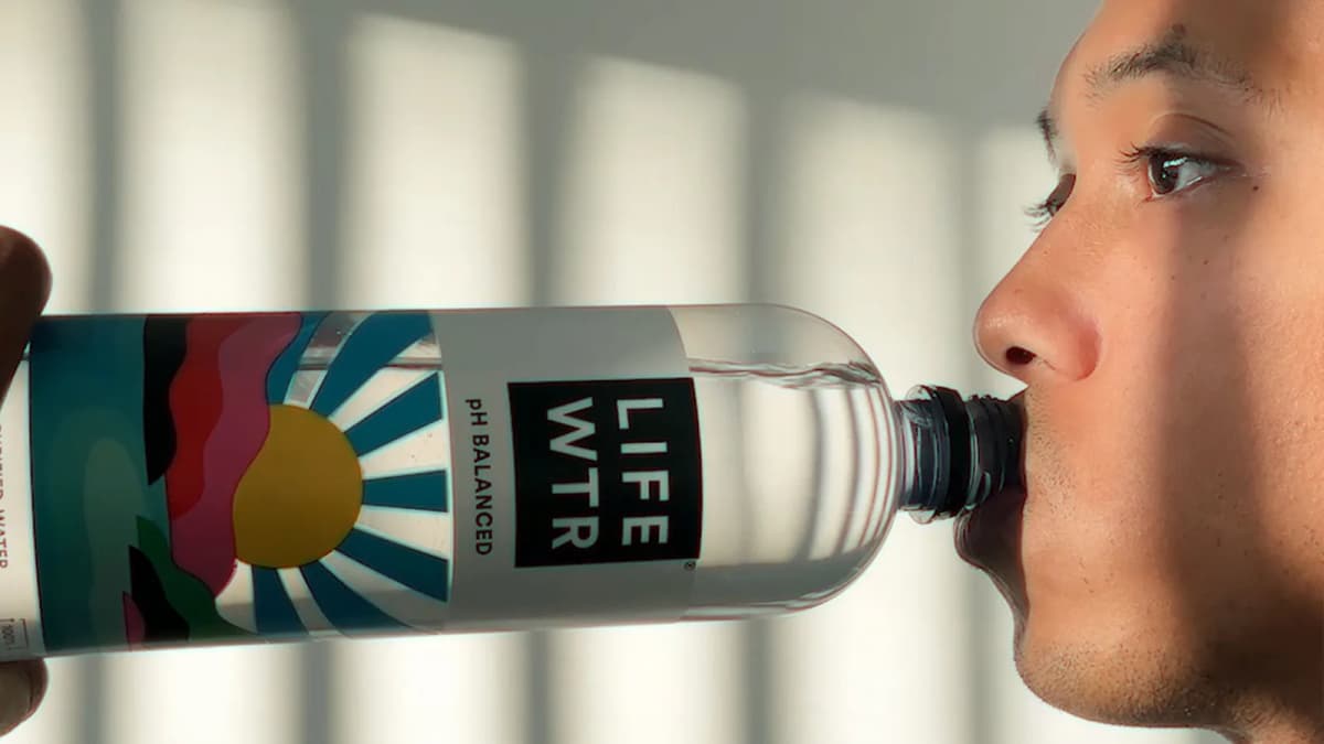 Close-up of a young man drinking from a clear water bottle with a colorful sunburst label reading "pH BALANCED"