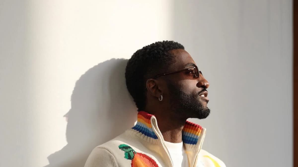 MATCHES, Pierre Laurent leaning on a wall in a cream zip cardigan with an orange knit motif