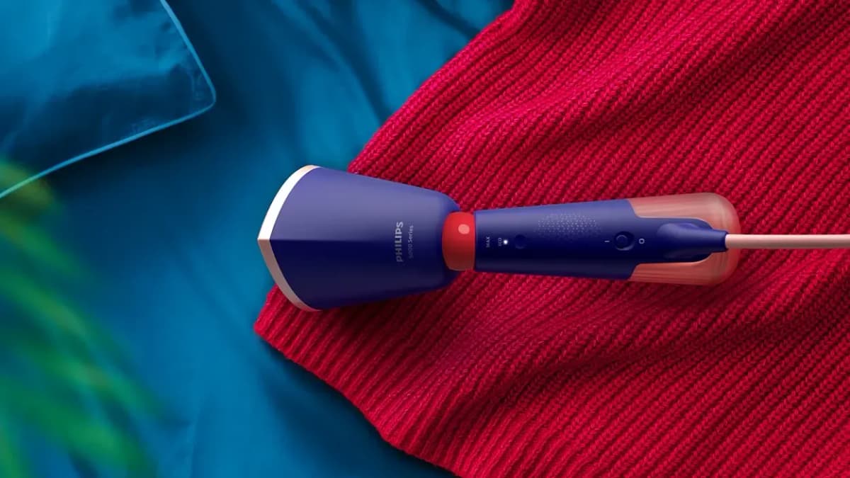 Purple Philips handheld steamer printed "PHILIPS" "5000 Series" lying on a red knit sweater beside teal fabric