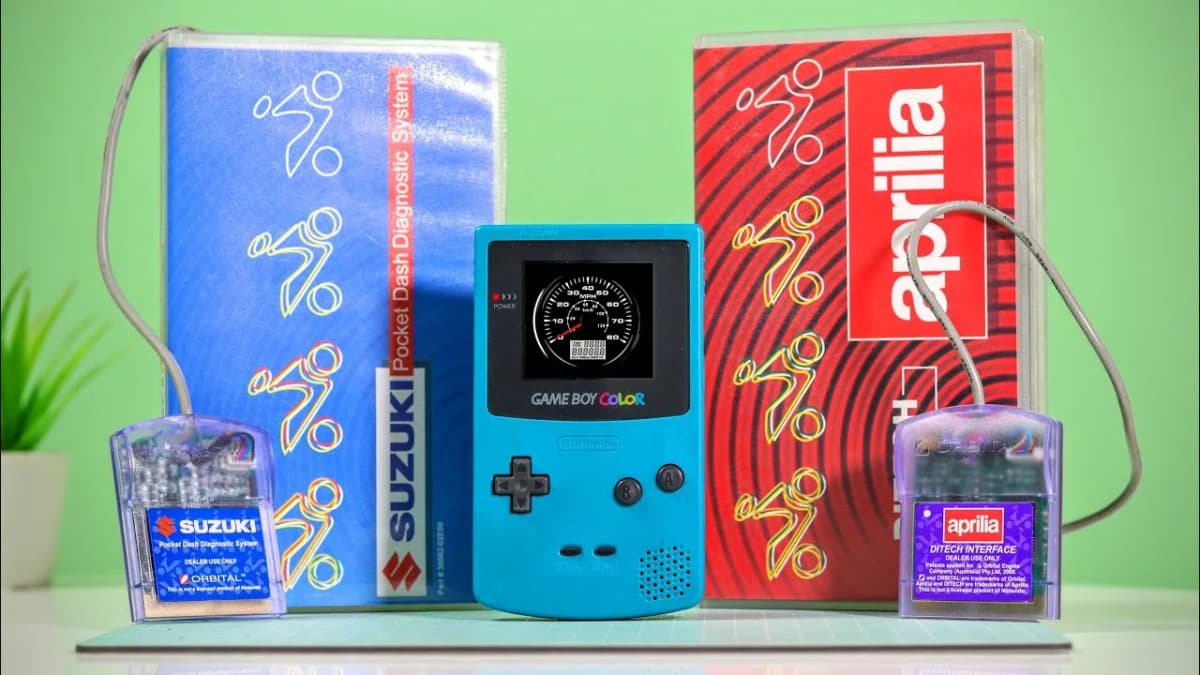 Teal handheld game console showing a speedometer, flanked by cabled diagnostic cartridges and their boxes