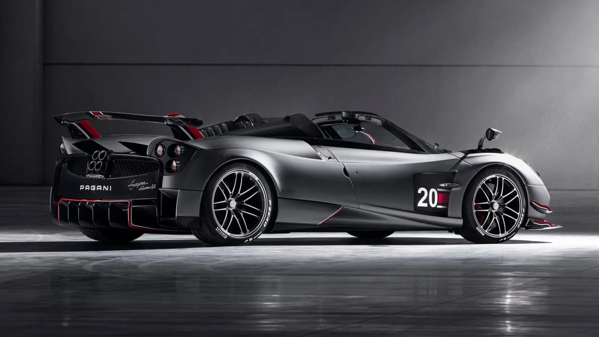 Matte grey Pagani roadster with "PAGANI" on the rear, red trim and number "20" on its side, parked in a dark studio