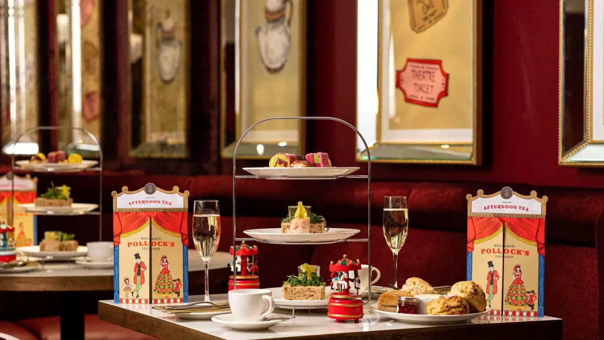 Afternoon tea stand with cakes, sandwiches and scones, champagne and "AFTERNOON TEA" menus on a table in a red room