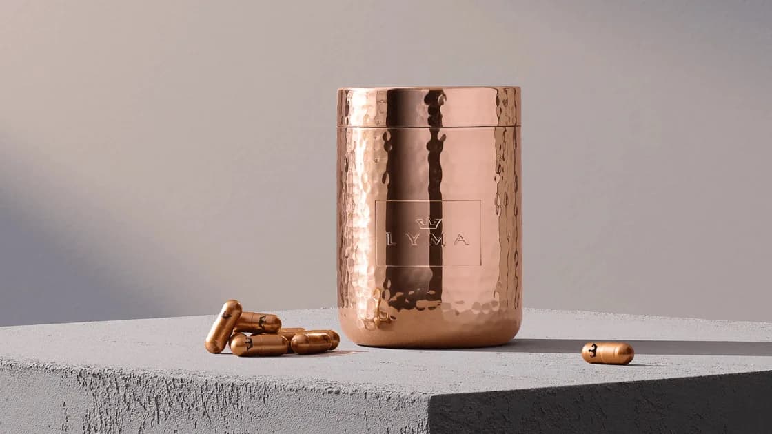 Hammered copper LYMA jar engraved "LYMA" beside scattered copper capsules on a gray concrete plinth