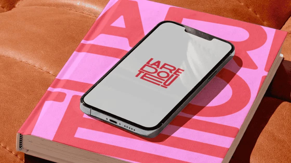 Smartphone showing the red La Redoute logo, resting on a pink and red book on a tan leather sofa